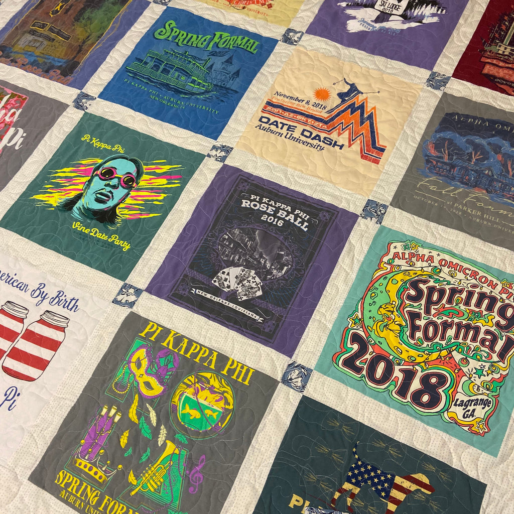A quilted patchwork blanket featuring multiple vintage T-shirt prints arranged in a grid, photographed laid flat on a carpeted floor. The design includes colorful graphic panels with text such as 'Spring Formal 2018,' 'Date Dash,' 'Pi Kappa Phi,' and 'America By Birth.