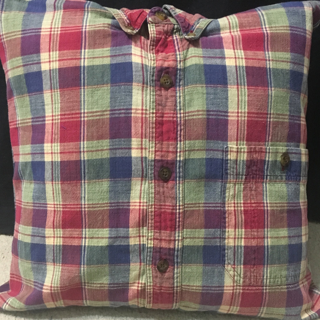 A square throw pillow made from a vintage plaid button-up shirt, featuring a red, blue, green, and beige plaid pattern with a chest pocket and button details.