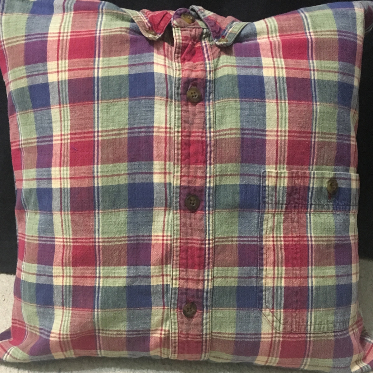 A square throw pillow made from a vintage plaid button-up shirt, featuring a red, blue, green, and beige plaid pattern with a chest pocket and button details.