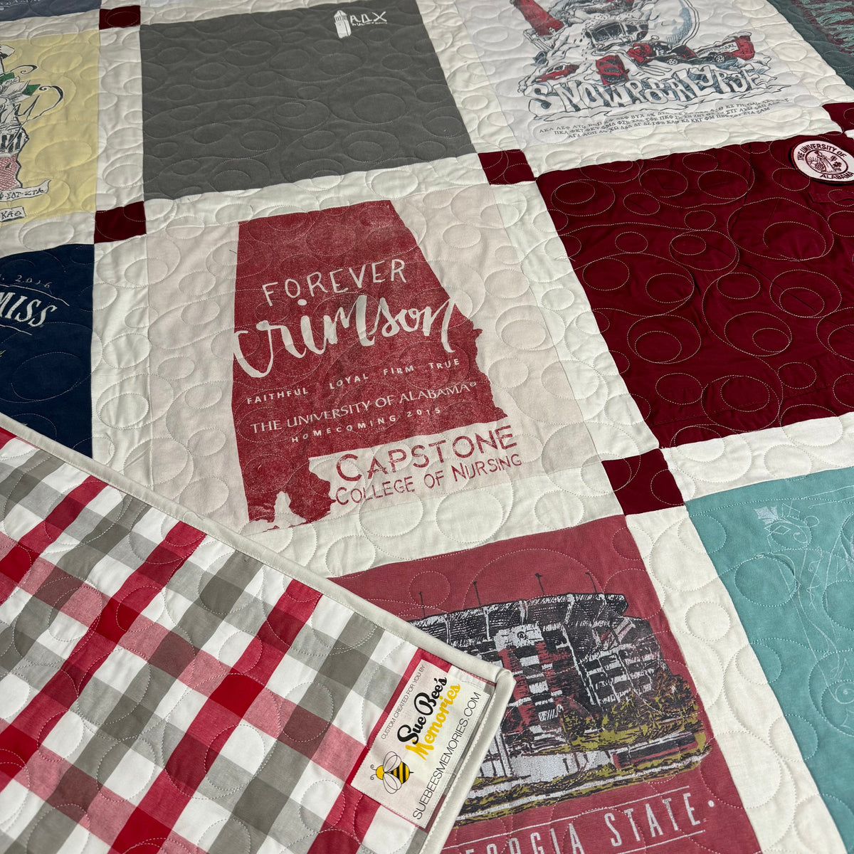 A quilted patchwork blanket featuring various collegiate-themed fabric squares, including a prominent red and white Georgia Crimson Tide design in the center and a red, white, and gray gingham pattern in the bottom left corner.