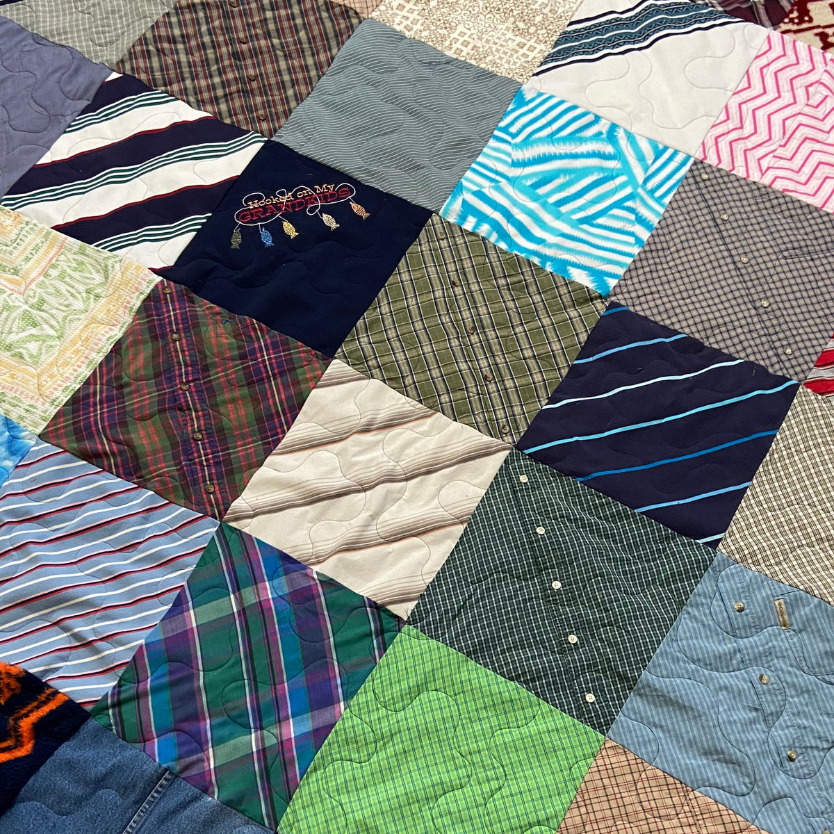 A handmade patchwork quilt made of various fabric squares in multiple colors and patterns, laid out on a beige carpeted floor.